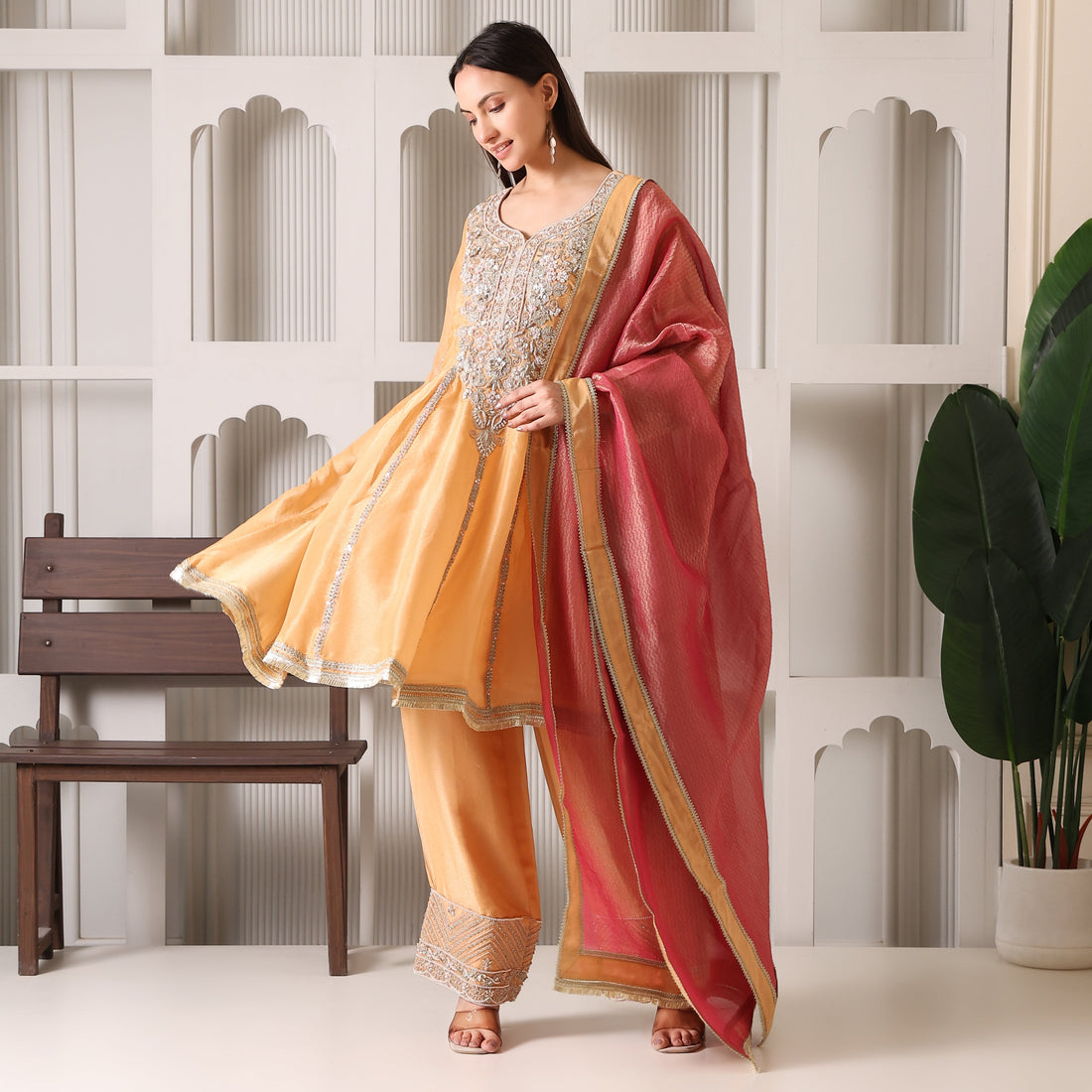 Woman in embroidered yellow Anarkali suit with pink dupatta, luxury ethnic wear indoors