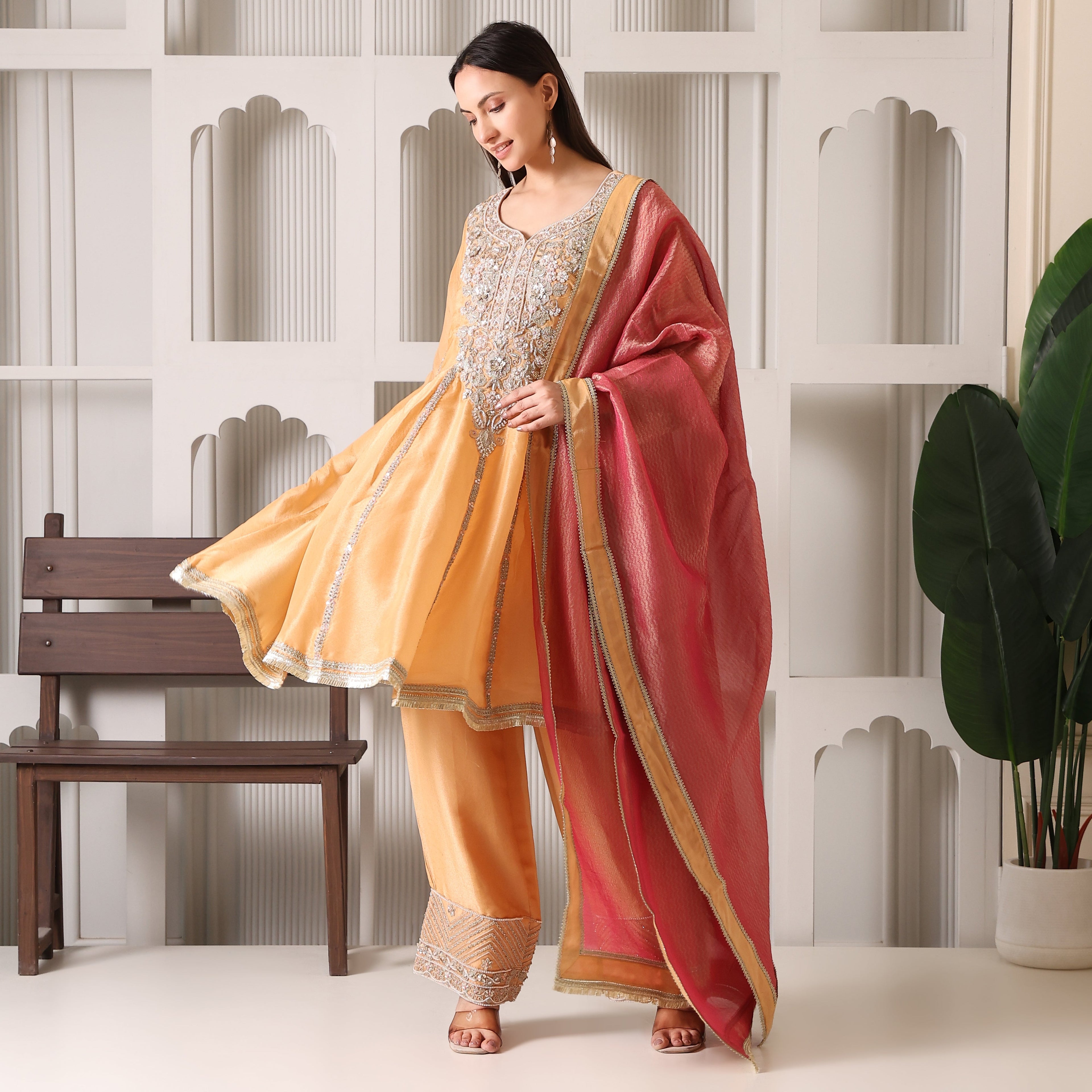 Woman in embroidered yellow Anarkali suit with pink dupatta, luxury ethnic wear indoors