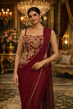 Woman wearing maroon designer saree with gold embroidery, traditional jewelry, in a luxurious setting