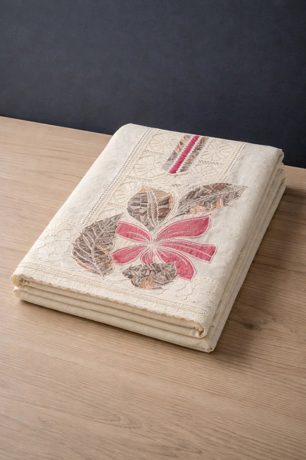 Cream-colored ethnic fabric with floral embroidery and lace detail, folded on a wooden surface