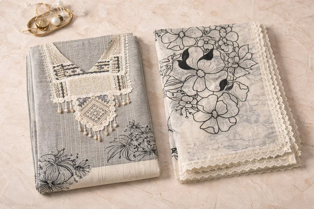 Elegant grey and white ethnic suit set with floral embroidery and lace, styled on marble surface.