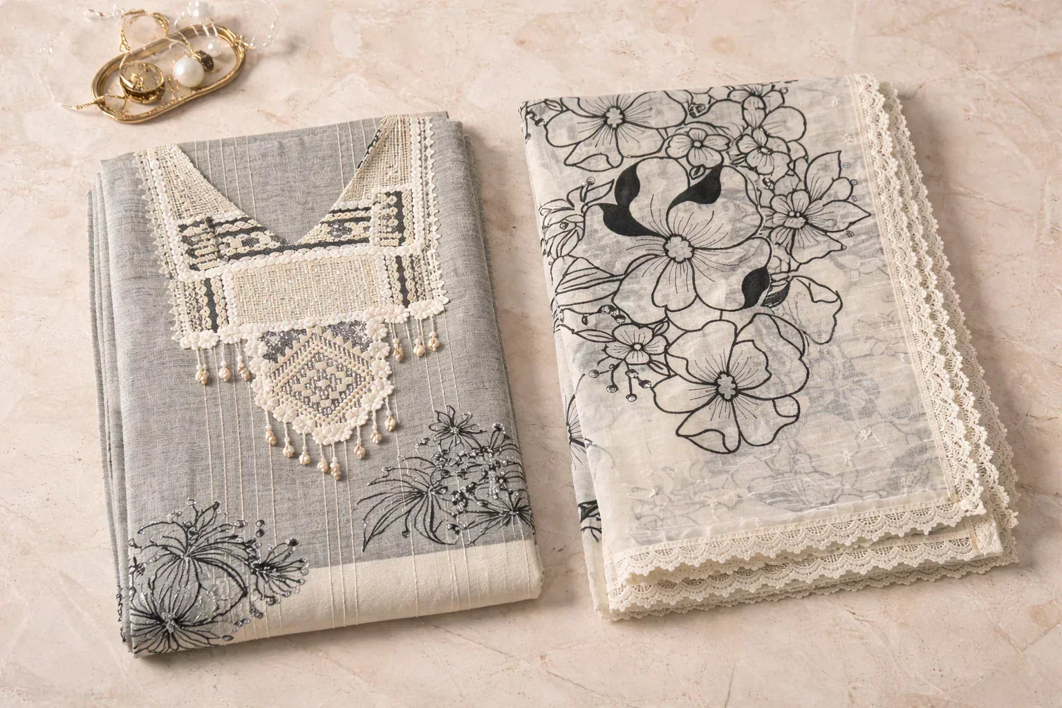 Elegant grey and white ethnic suit set with floral embroidery and lace, styled on marble surface.