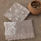 Embroidered beige ethnic fabric with floral patterns and lace border, displayed on stone