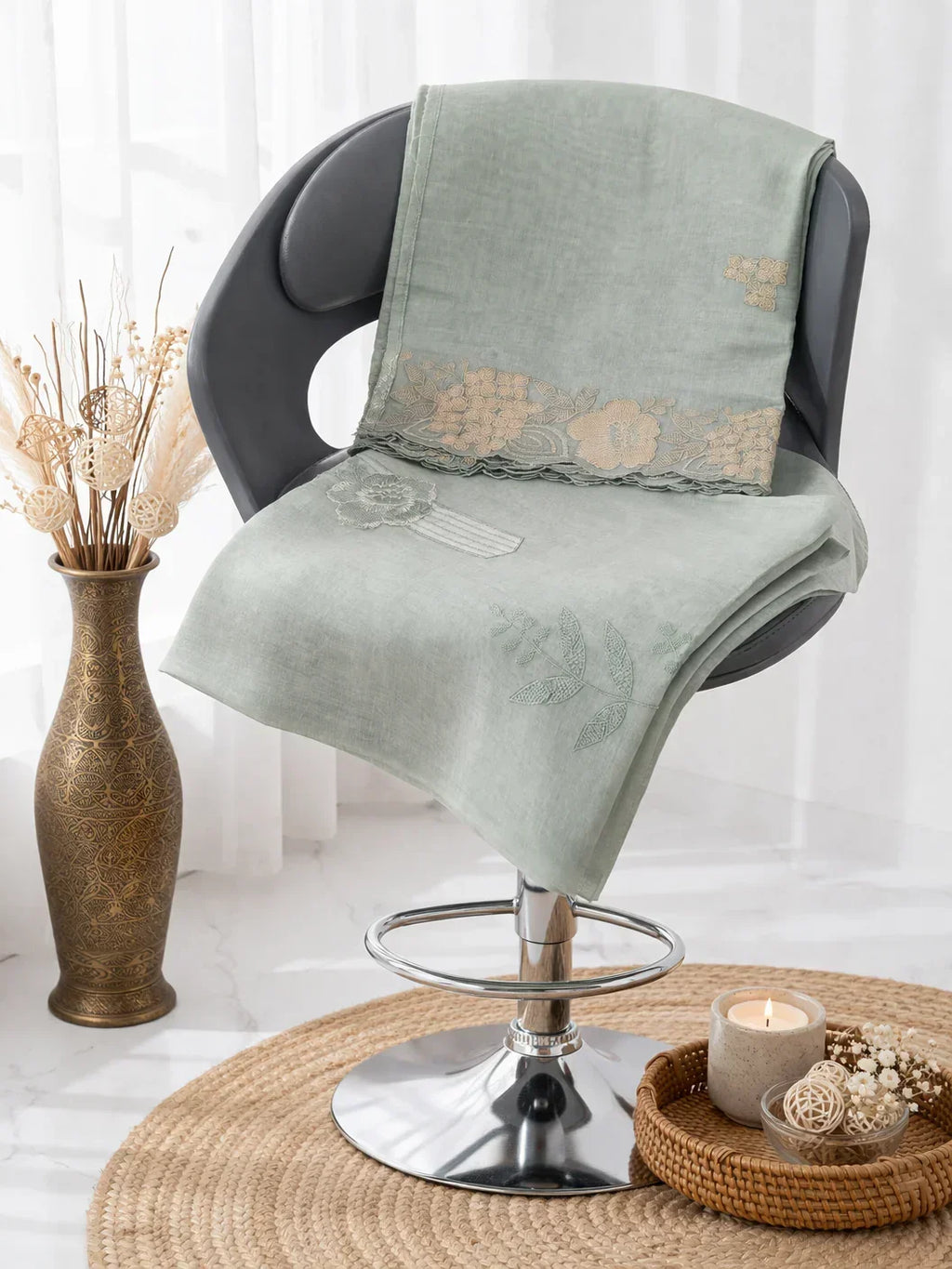 Light green embroidered ethnic fabric draped on a chair, floral vase and candle decor nearby