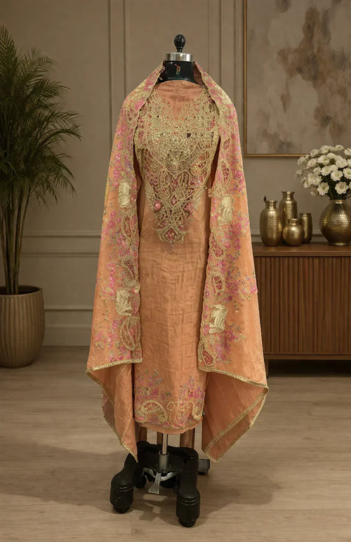 Embroidered peach ethnic suit with ornate dupatta, displayed on mannequin in elegant room.