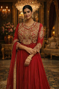 Woman in elegant red Anarkali suit with gold embroidery, wearing ethnic jewelry, in a luxurious setting