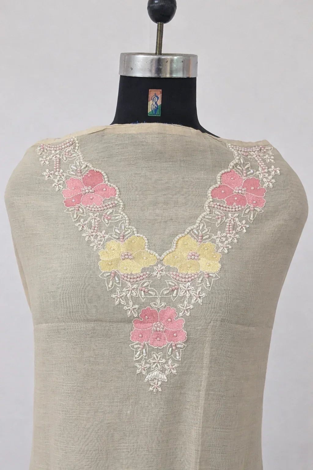 Beige ethnic fabric with pink and yellow floral embroidery on neckline, displayed on mannequin