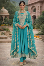 Woman in teal Banarasi Anarkali suit with gold embroidery, traditional jewelry, outdoor setting