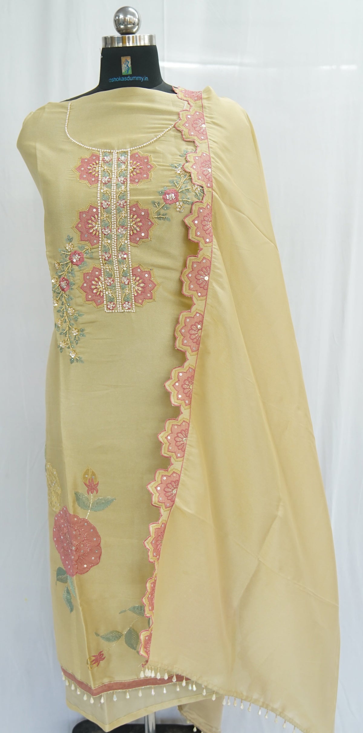 A light yellow ethnic salwar suit set displayed on a black mannequin, featuring a kurta with pink floral embroidery, a matching dupatta with scalloped pink border, and a black base stand.