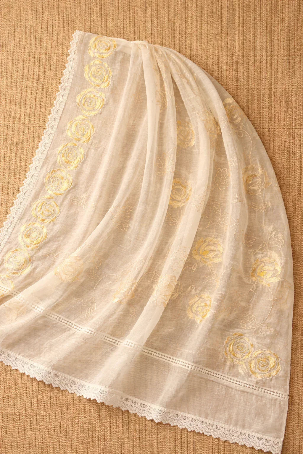 Sheer cream dupatta with gold floral embroidery and lace border on beige background