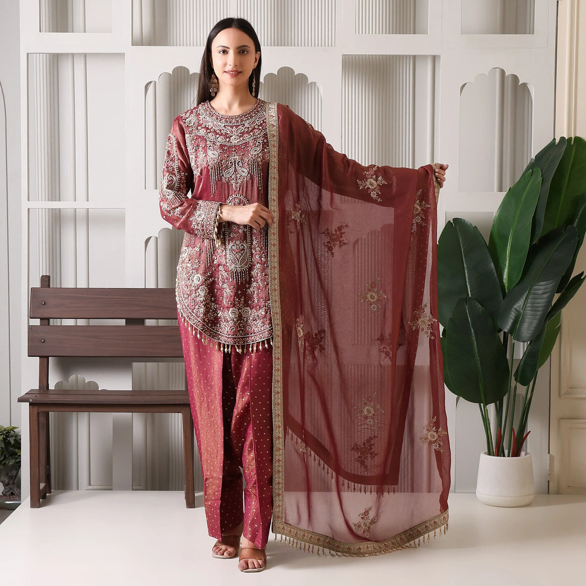 Woman in maroon embroidered ethnic suit with matching dupatta, festive indoor setting