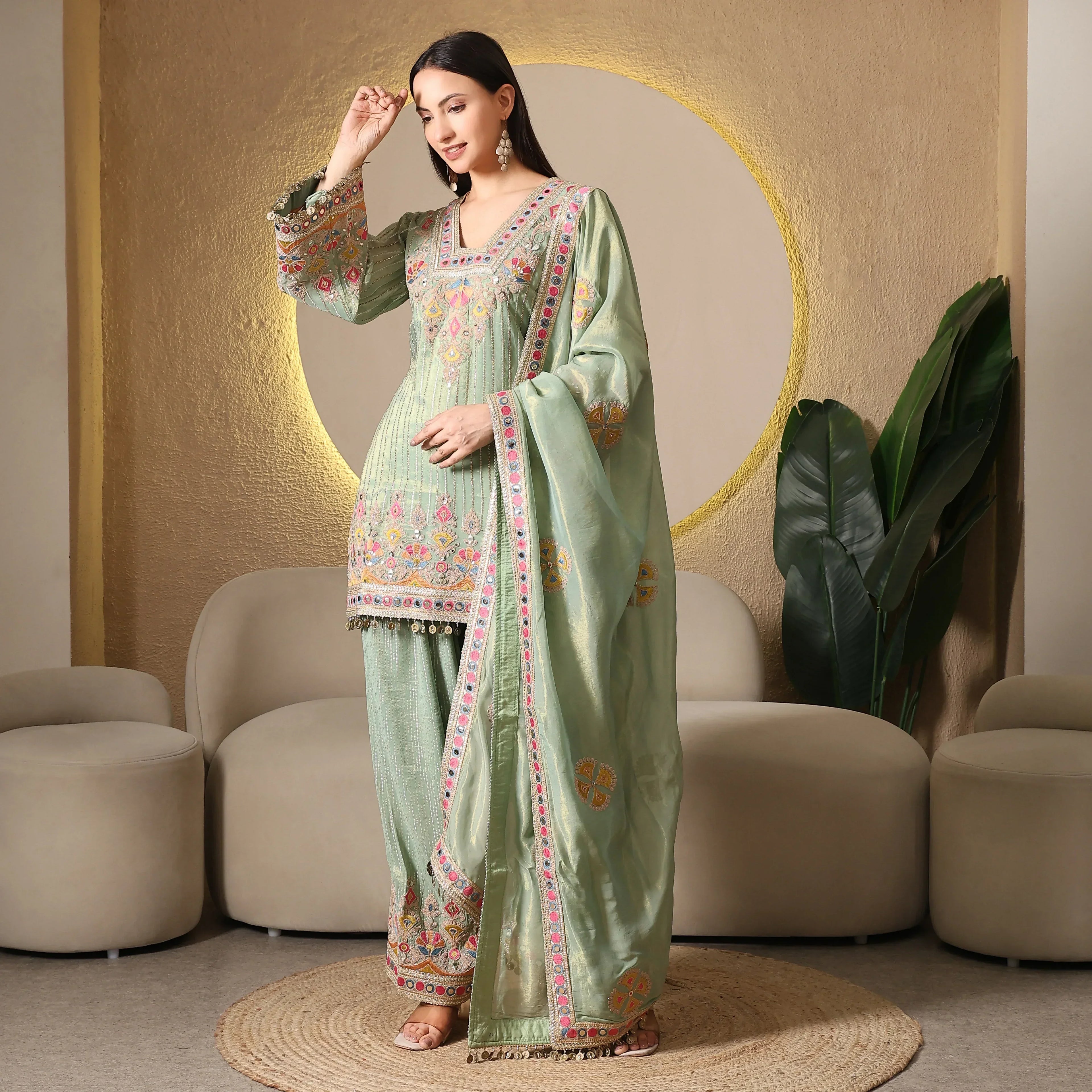 Woman wearing pastel green embroidered ethnic suit with matching dupatta, in modern living room