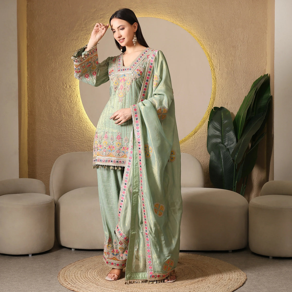 Woman wearing pastel green embroidered ethnic suit with matching dupatta, in modern living room