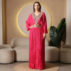Woman in a fuchsia pink embellished ethnic suit with pleated skirt, standing in modern living room