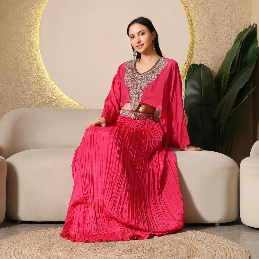 Woman in a vibrant pink ethnic embellished skirt set, seated on a beige sofa, modern decor
