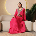 Woman in a vibrant pink ethnic embellished skirt set, seated on a beige sofa, modern decor