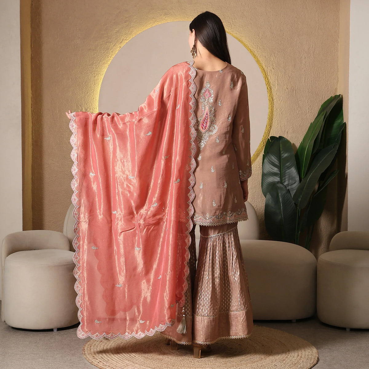 Woman wearing an embroidered ethnic suit with peach dupatta and flared pants, back view