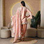 Woman in pastel pink ethnic suit with embroidered dupatta, standing in modern lounge