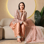 Woman in peach embroidered ethnic suit with dupatta, seated on beige sofa, festive setting