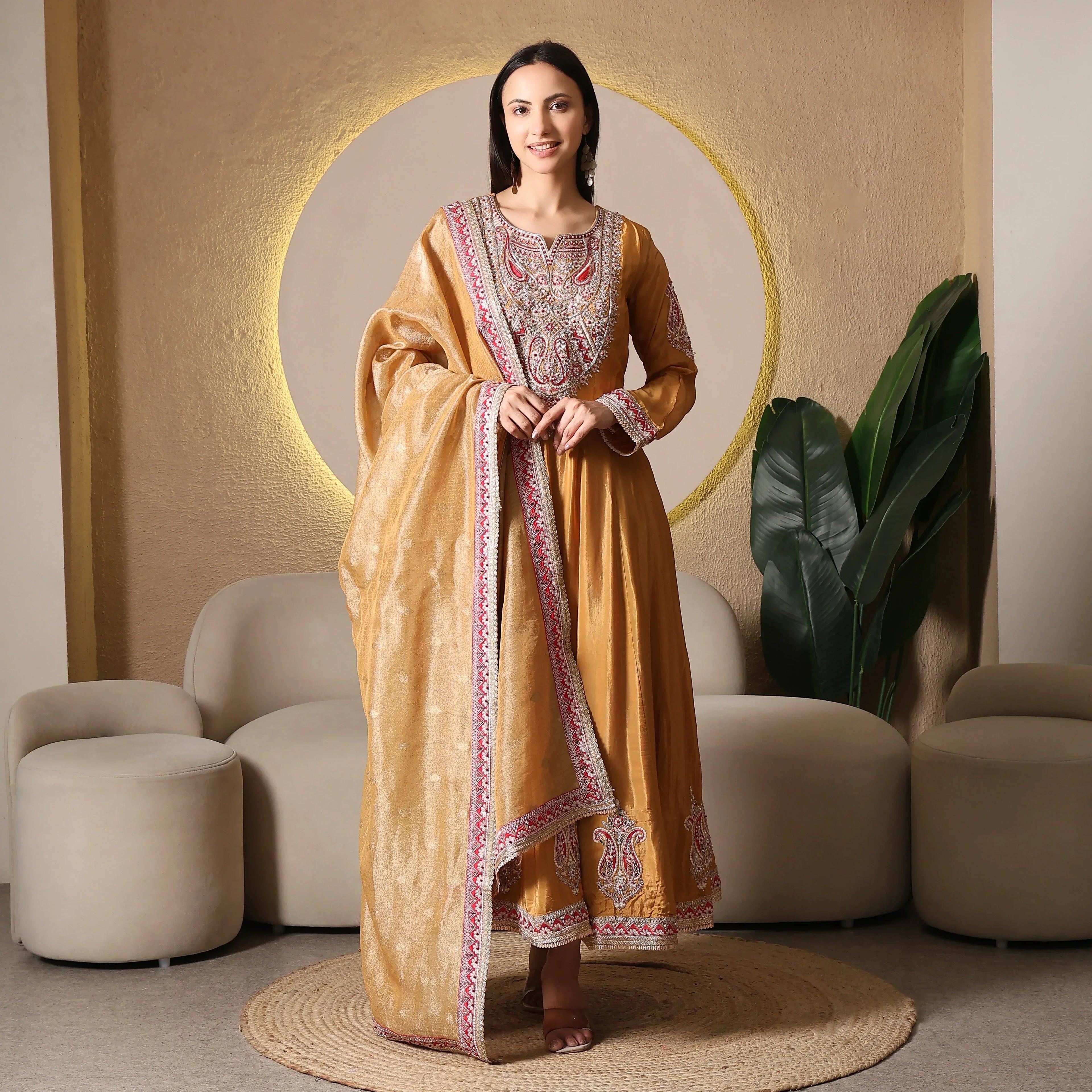 Woman wearing mustard Banarasi Anarkali suit with dupatta, traditional embroidery, indoor setting