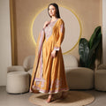 Woman wearing a mustard yellow embroidered Anarkali suit with dupatta, standing in a modern living room.