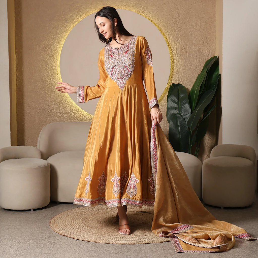 Woman wearing embroidered golden Anarkali suit with dupatta in modern ethnic living room