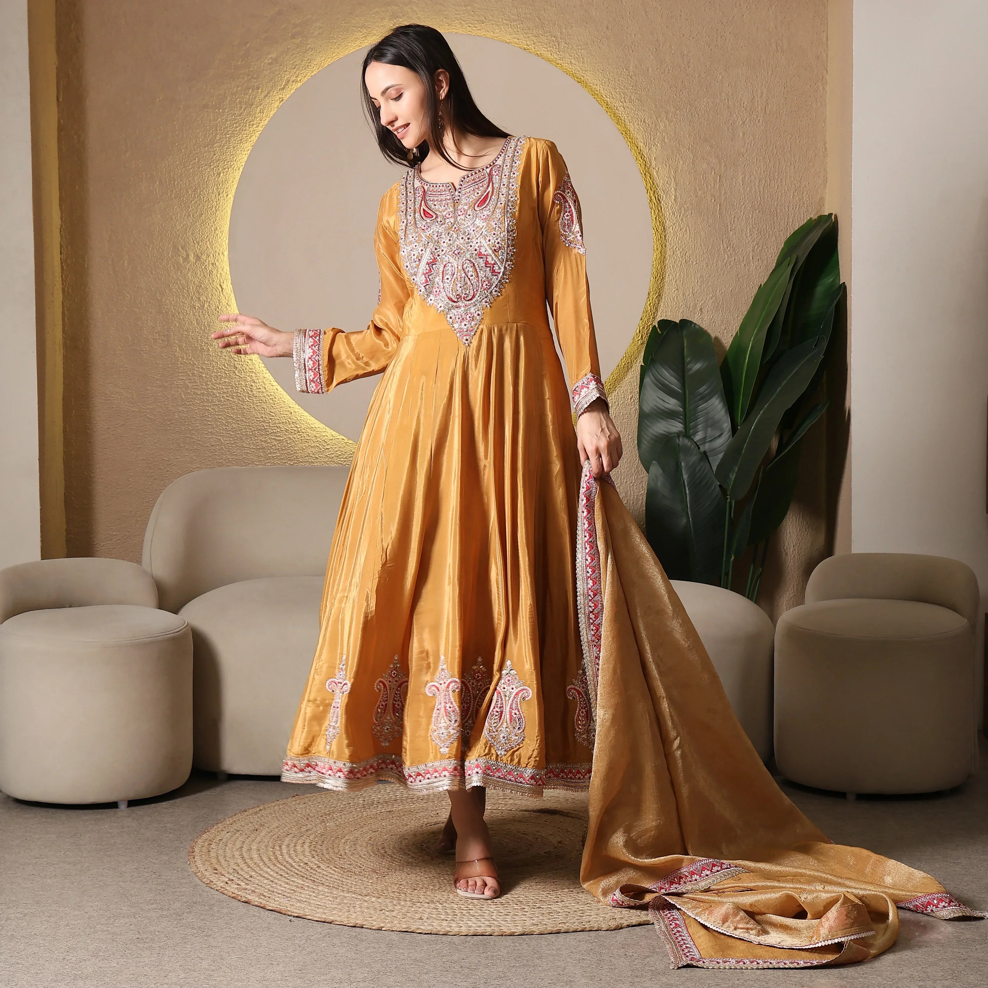 Woman wearing embroidered golden Anarkali suit with dupatta in modern ethnic living room