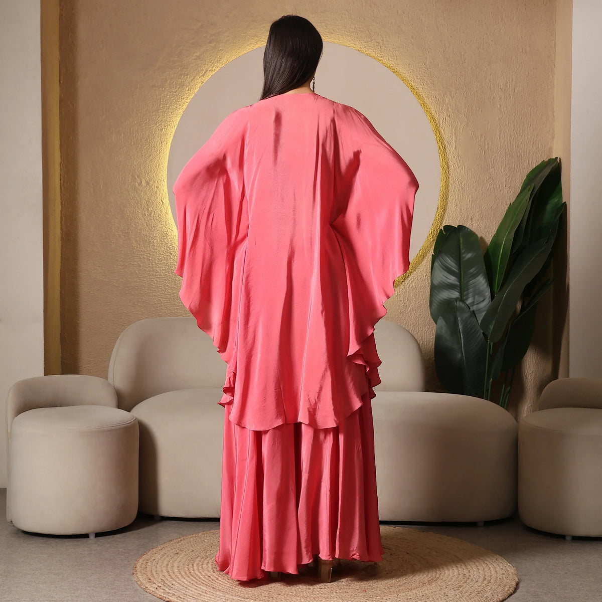Woman in flowy pink ethnic gown with cape sleeves, standing in modern, elegant room