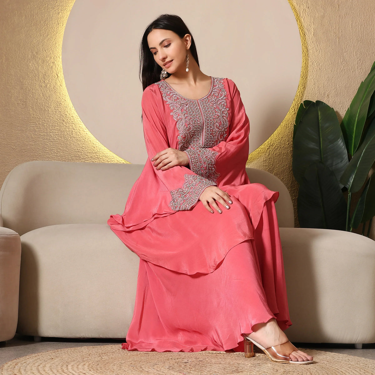 Woman seated on sofa wearing pink ethnic Anarkali suit with silver embroidery, festive wear