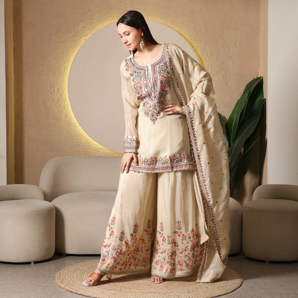Woman wearing cream embroidered ethnic palazzo suit with dupatta in elegant indoor setting