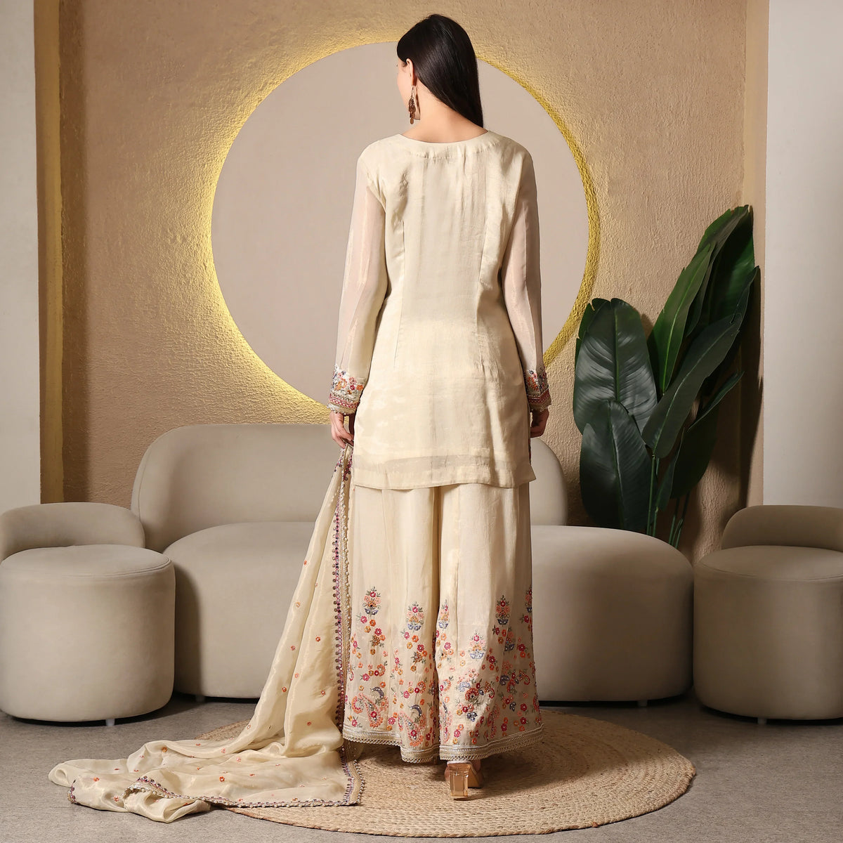 Woman in cream ethnic suit with floral embroidery and dupatta, standing indoors