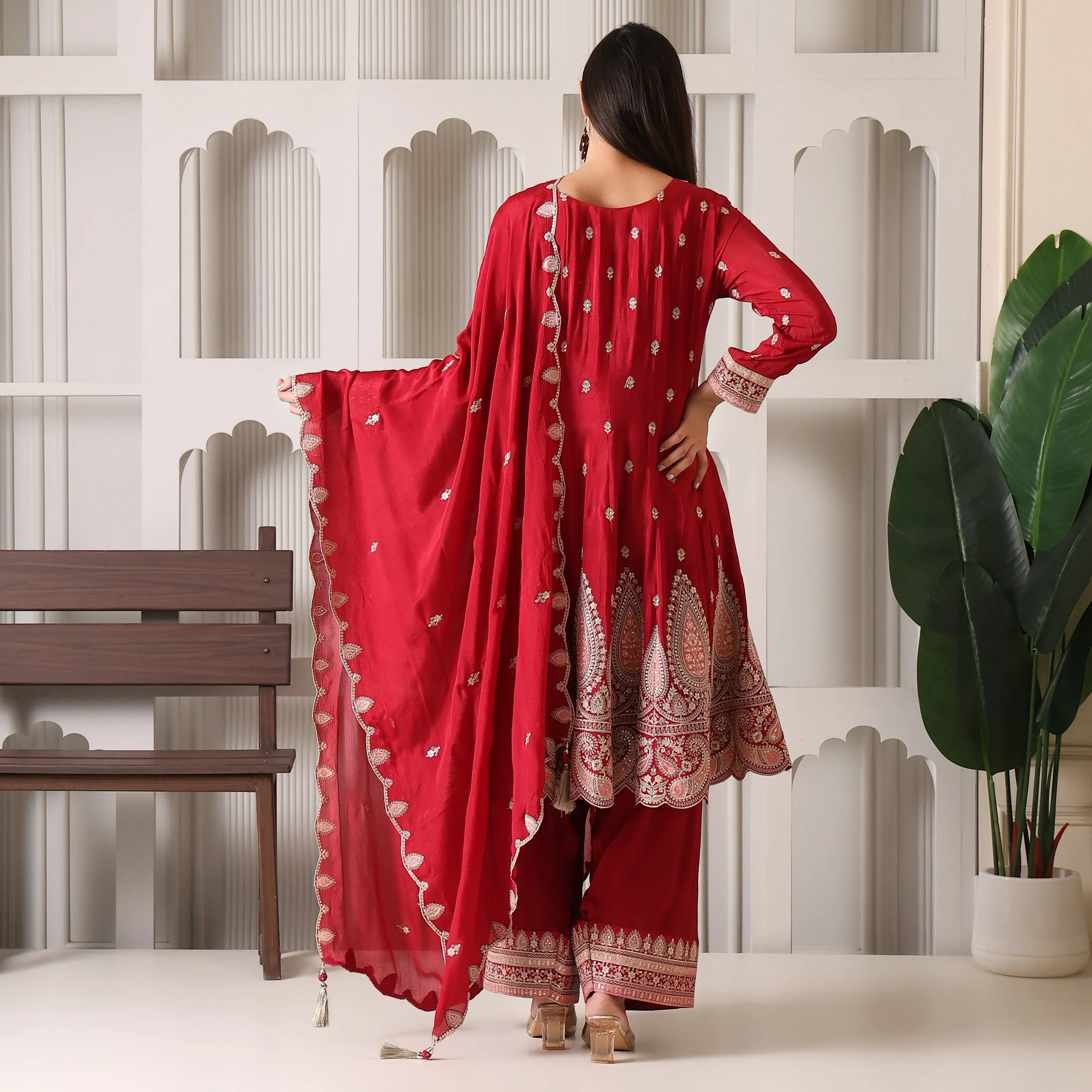 Woman in red embroidered Anarkali suit with dupatta, standing indoors, festive ethnic wear