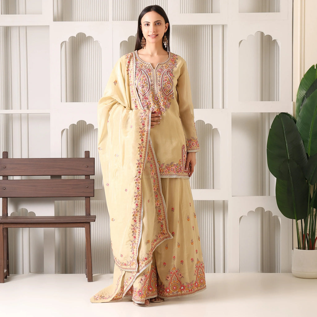Woman wearing beige Banarasi Anarkali suit with floral embroidery and dupatta indoors