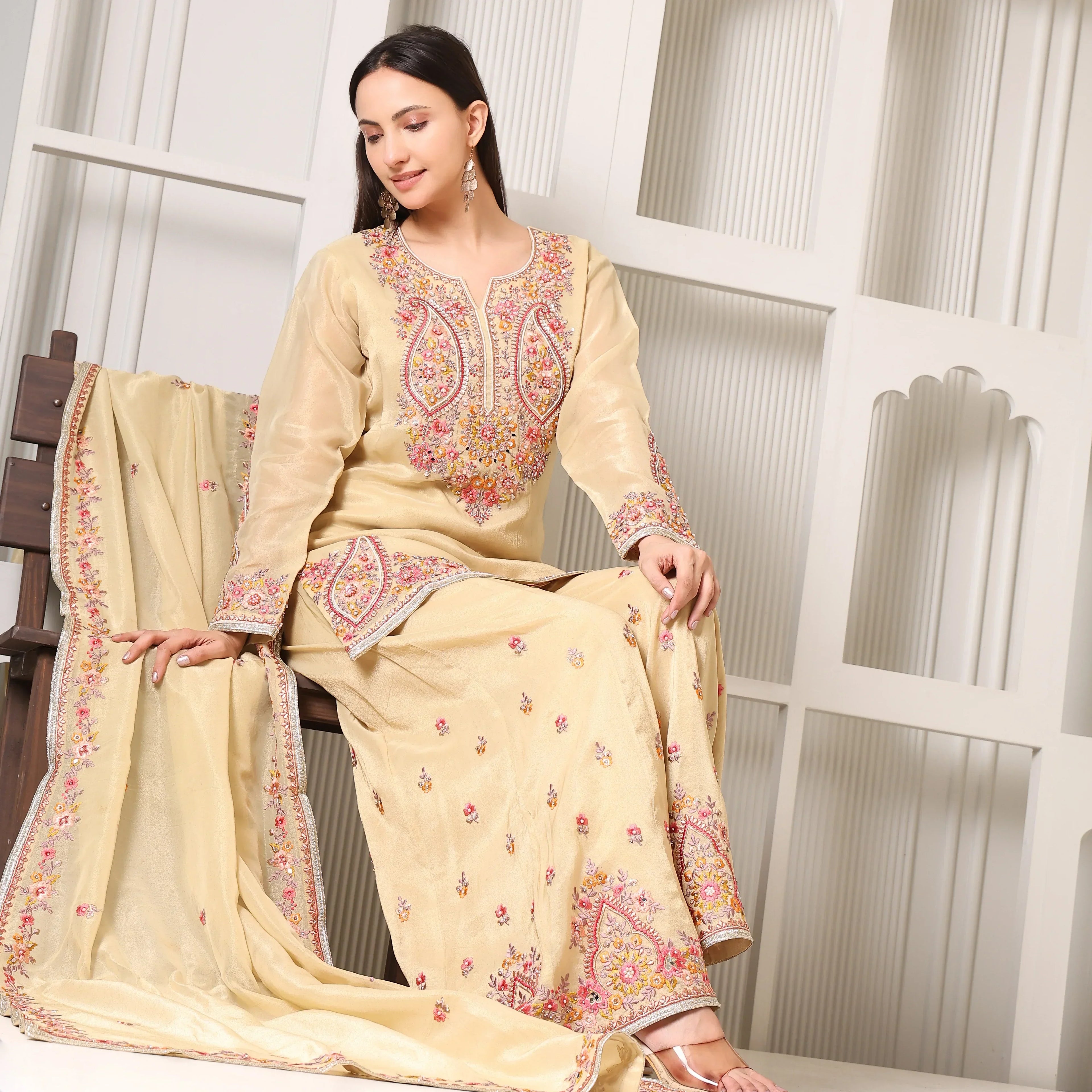 Woman in cream Banarasi Anarkali suit with pink floral embroidery, sitting indoors