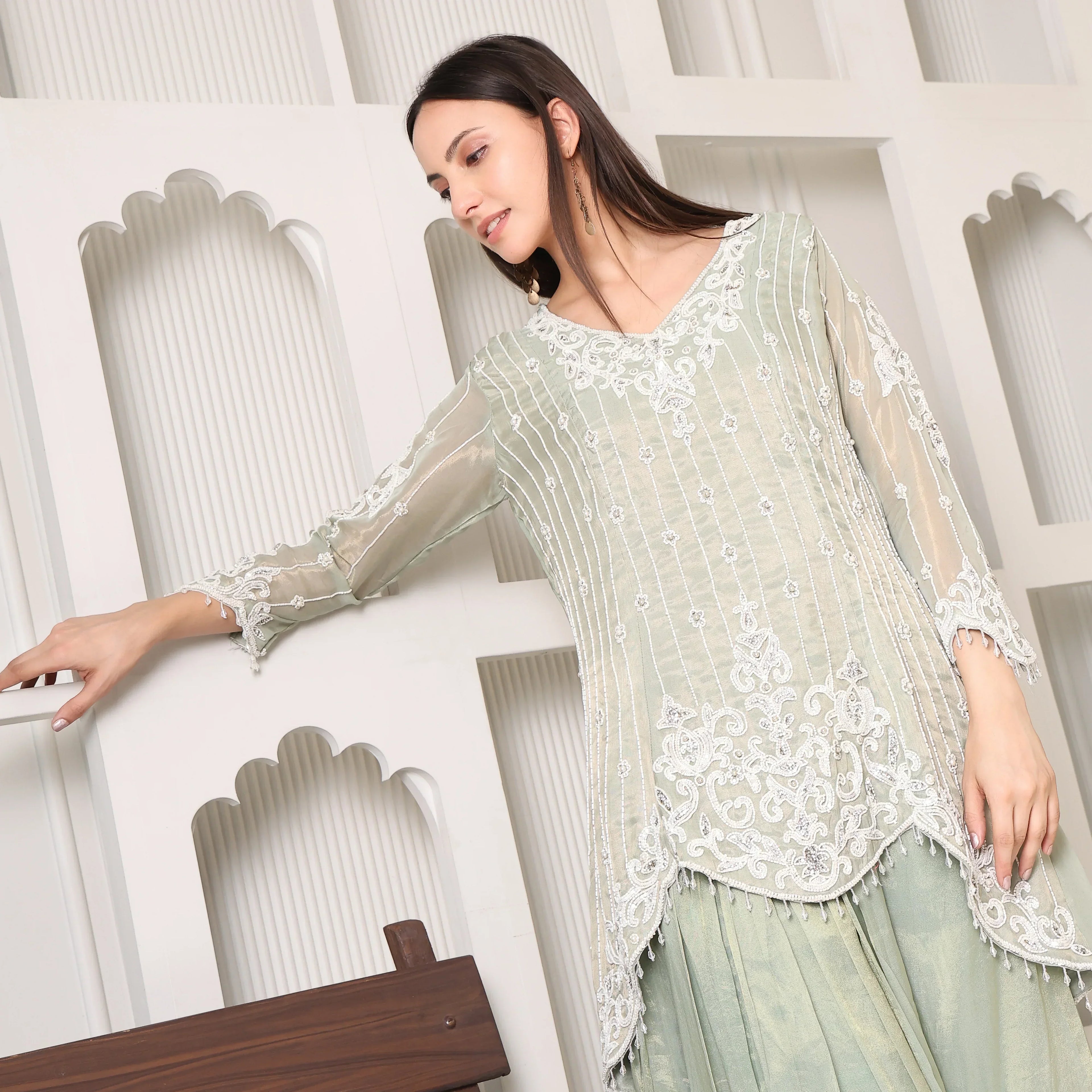 Woman in elegant pastel green embroidered Anarkali suit with sheer sleeves and traditional decor