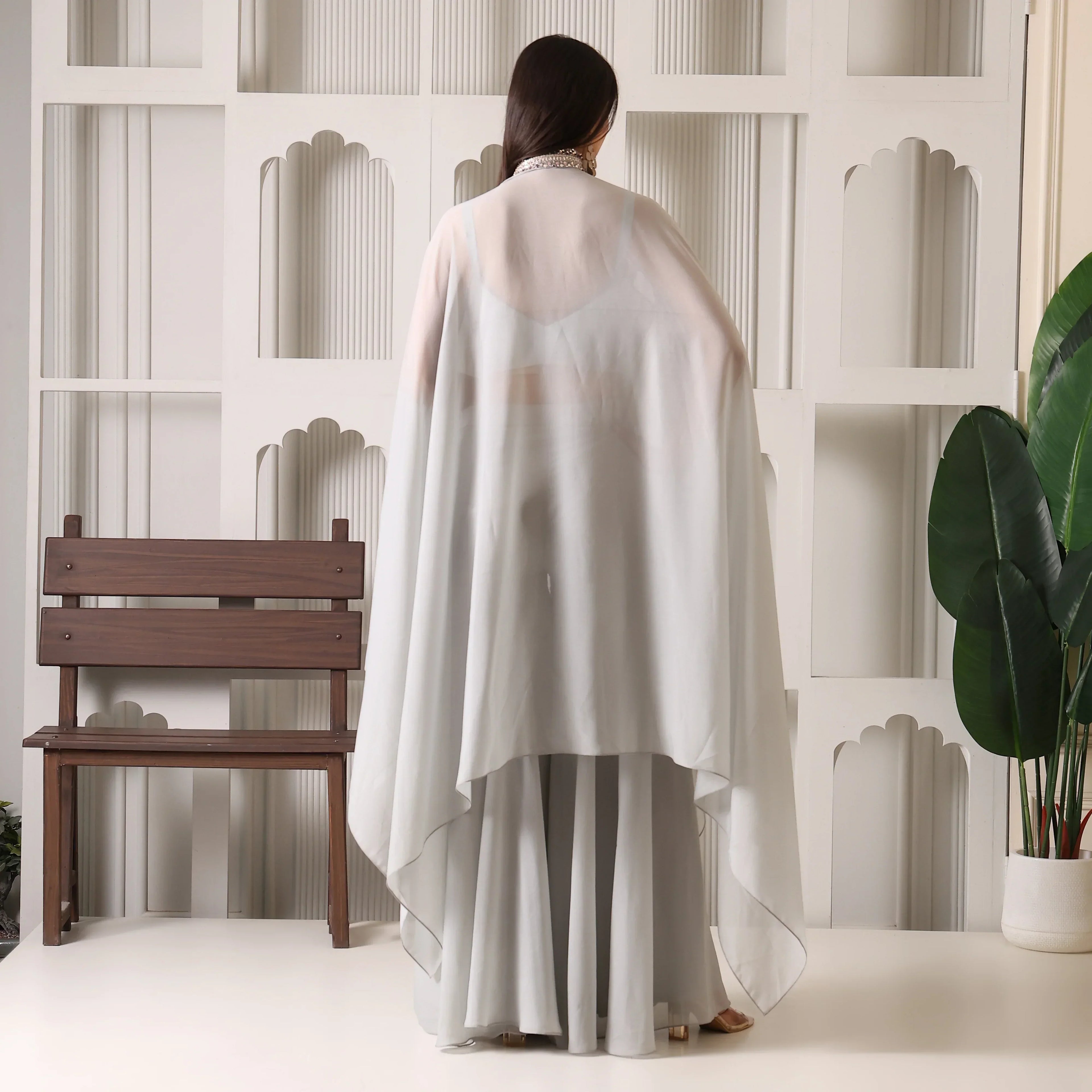 Woman in light grey ethnic cape set facing away, flowy dupatta, indoor modern decor