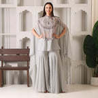 Woman in a grey designer ethnic suit with embellished cape and flared pants, indoor setting