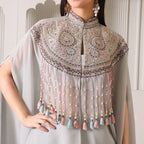 Woman wearing a pastel embroidered cape with tassels and beads, styled for festive occasions
