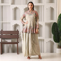 Woman wearing a beige Anarkali suit with floral embroidery, standing indoors.