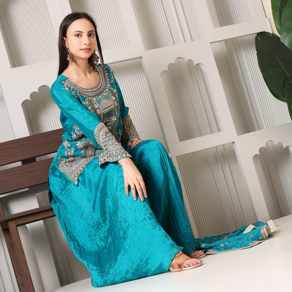 Woman in turquoise embroidered ethnic suit sitting on bench, wearing traditional festive wear
