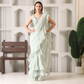 Woman in a pastel green ruffle saree with embroidered blouse, posing indoors