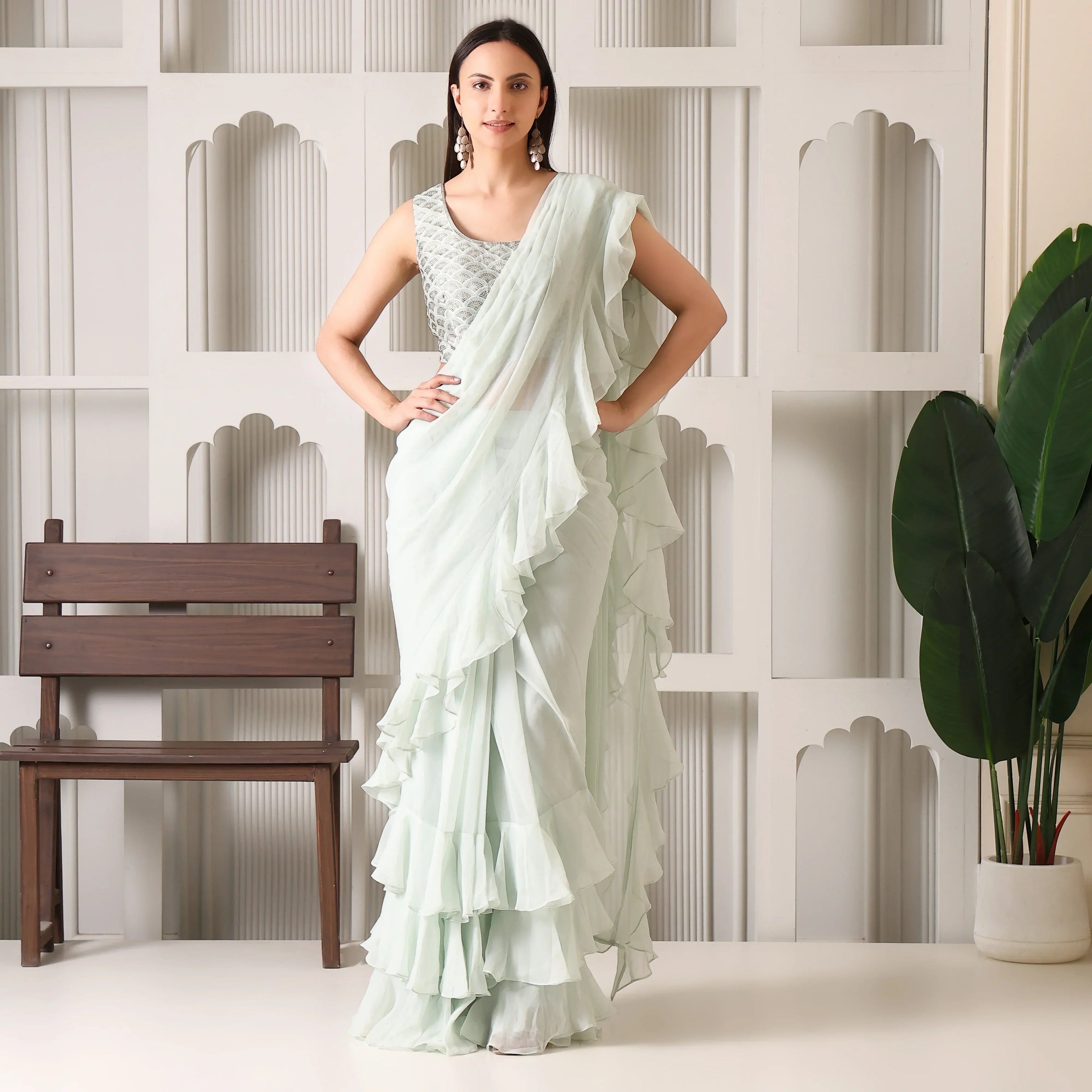 Woman in a pastel green ruffle saree with embroidered blouse, posing indoors