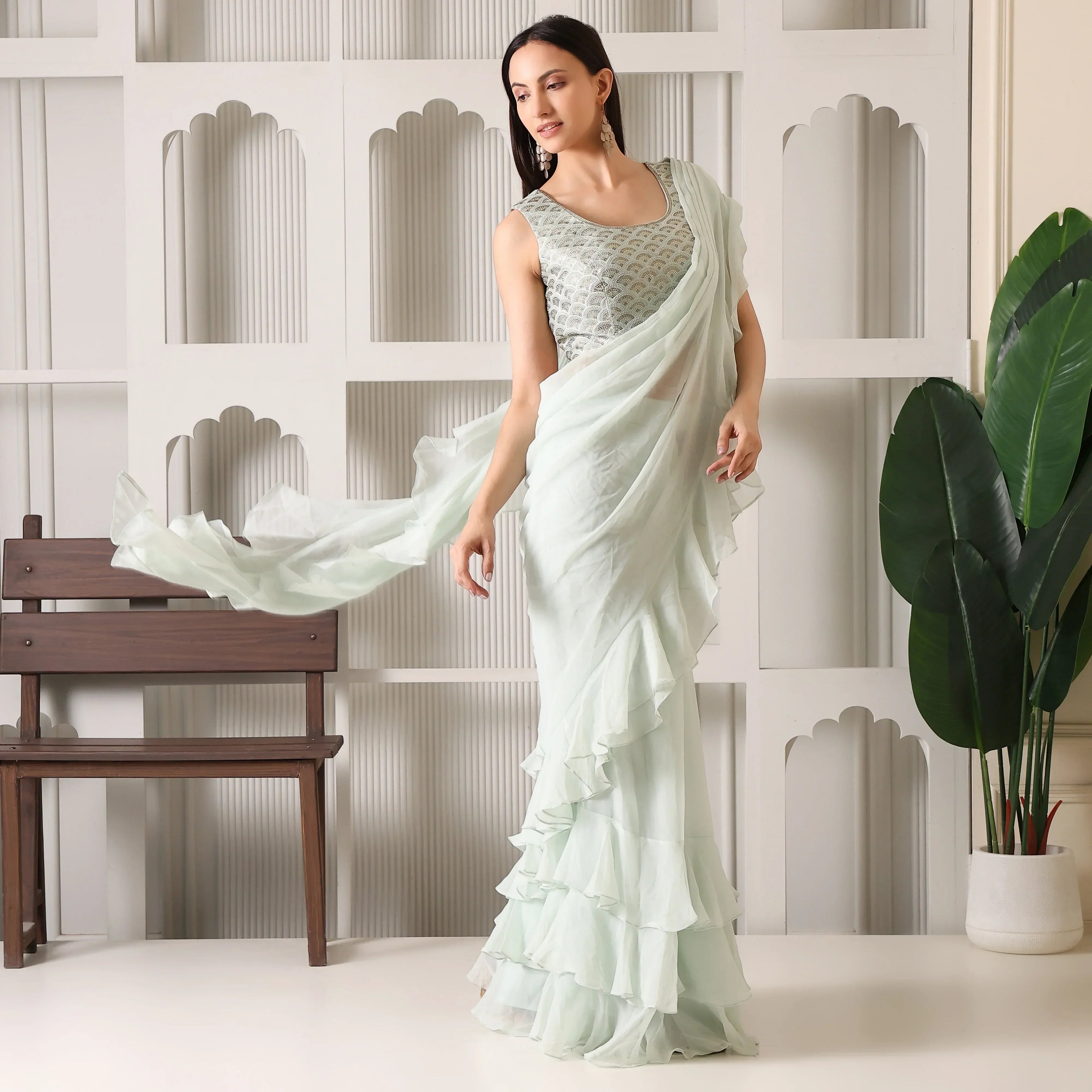 Woman in mint green ruffle saree and sleeveless embroidered blouse in elegant indoor setting