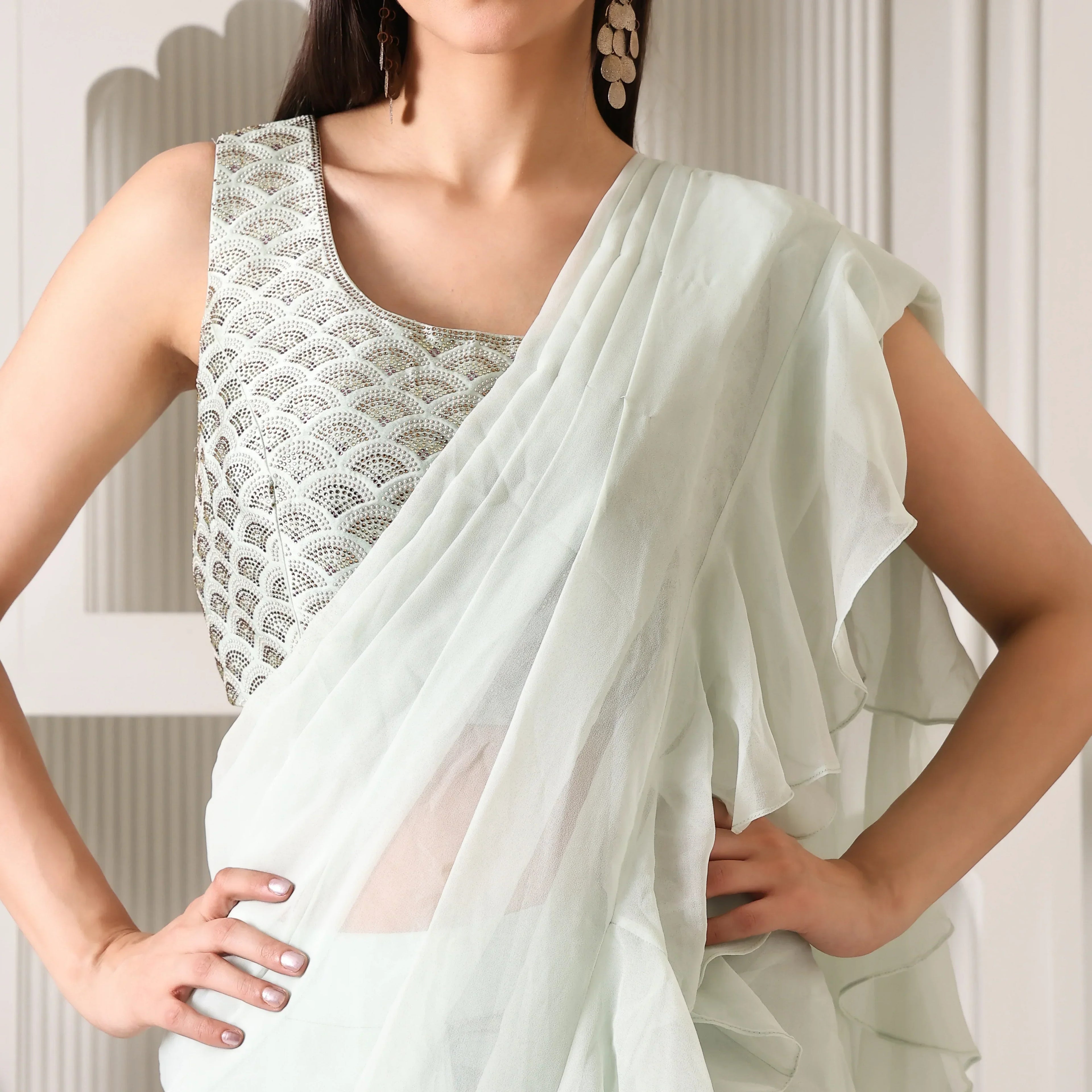 Woman in pastel green designer saree with sleeveless embroidered blouse, elegant ethnic wear