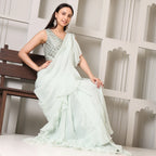 Woman in pastel green designer saree with embroidered blouse, sitting on a bench indoors