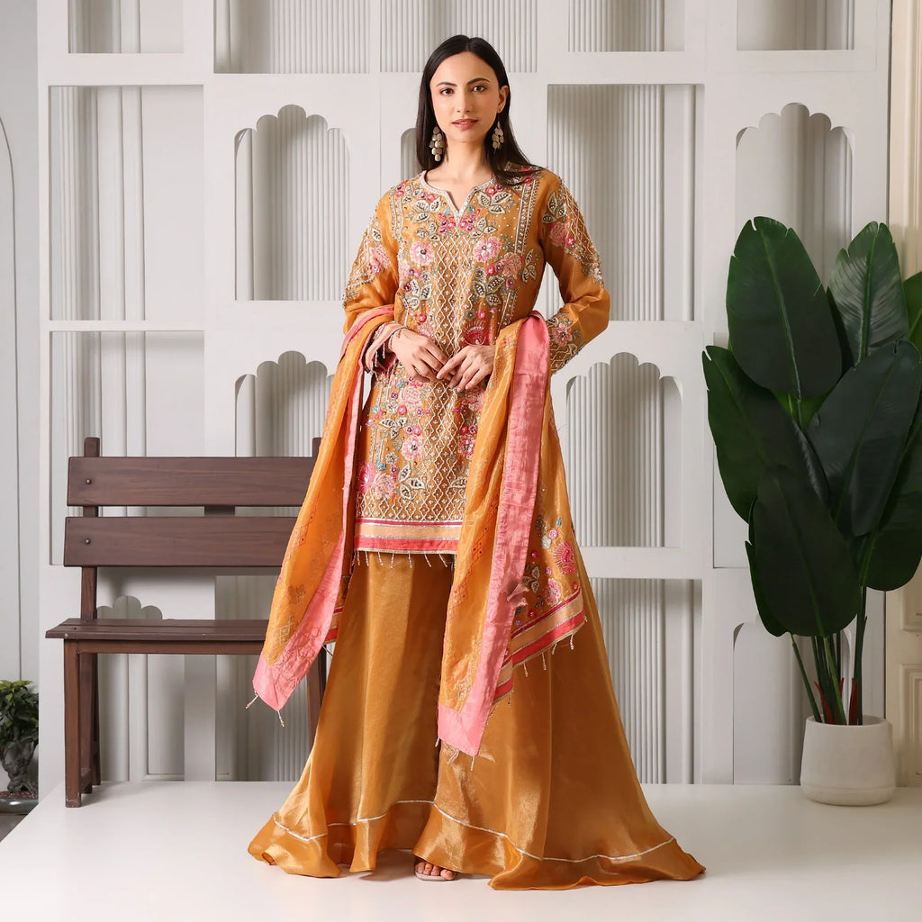 Woman in a gold and pink Banarasi Anarkali suit with embroidery, holding matching dupatta