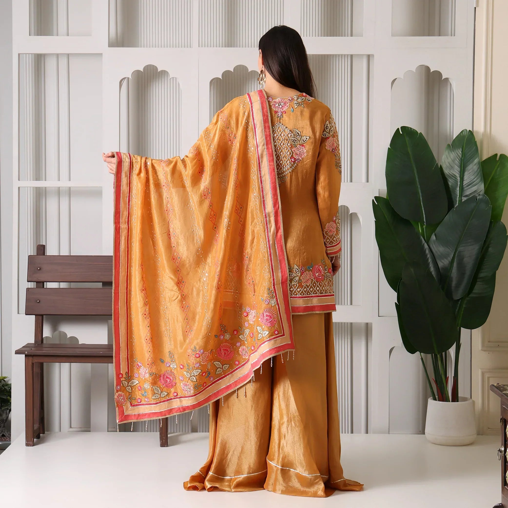 Woman in gold and orange ethnic suit set with floral embroidery and dupatta, back view