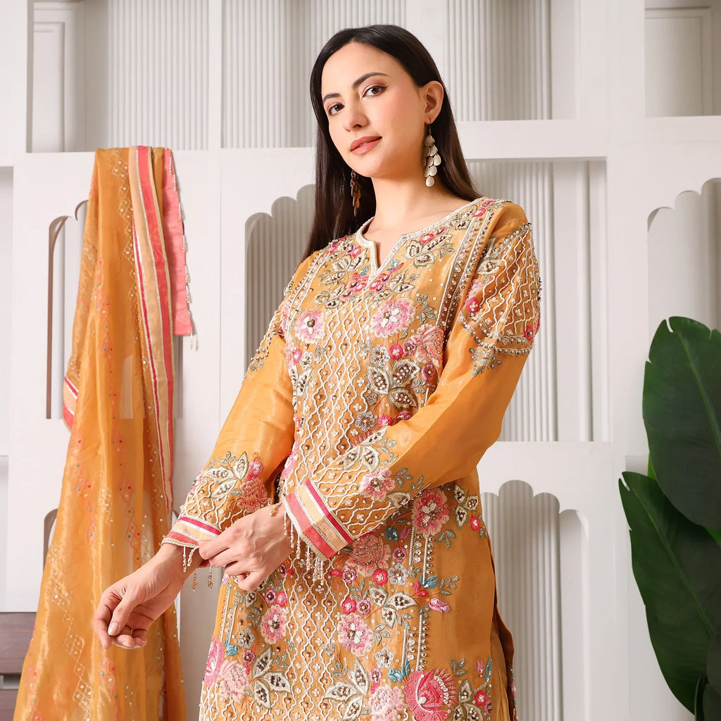 Woman wearing mustard yellow Banarasi Anarkali suit with floral embroidery, dupatta in background