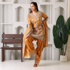 Woman in mustard yellow embroidered ethnic suit with dupatta, posing indoors near a bench and potted plant