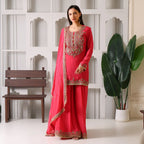 Woman wearing a pink embroidered ethnic suit with dupatta, standing indoors by plants
